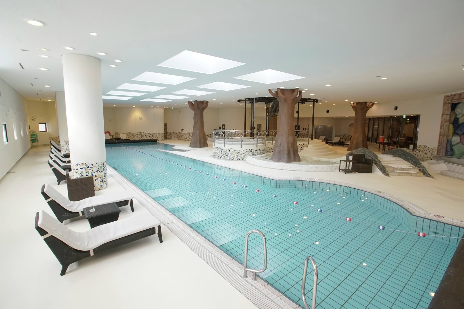 Sotokoto Club indoor pool with deck chairs and palm trees inside the glass-roofed atrium