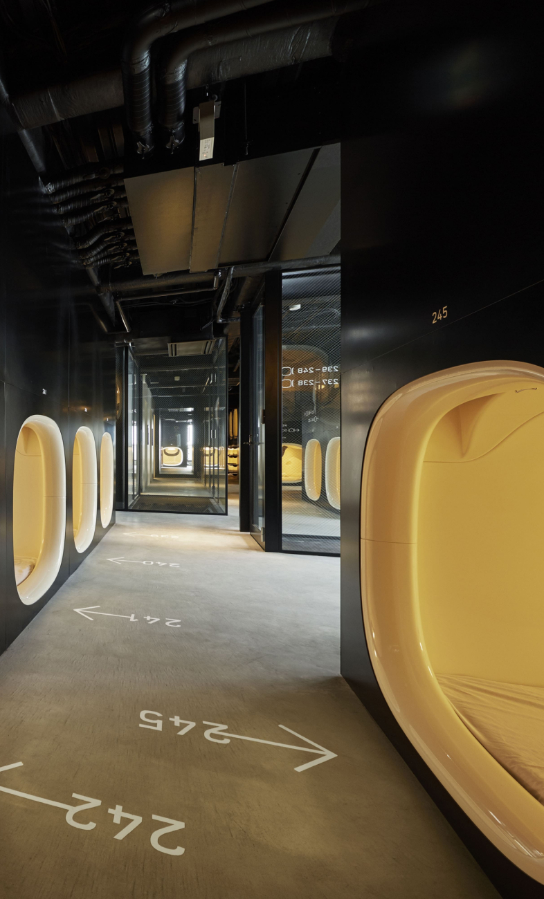 9h nine hours capsule hotel pod corridor — numbered yellow pods stacked two high in a black-walled hallway