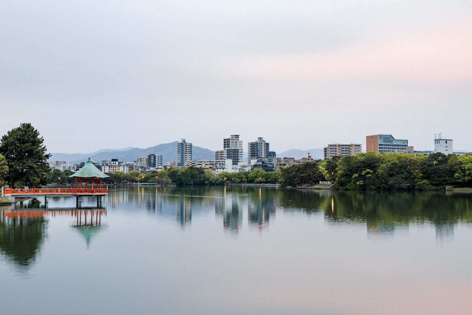 Ohori Park lake at dusk with the traditional Nakashima teahouse bridge reflected in still water, Fukuoka skyline beyond
